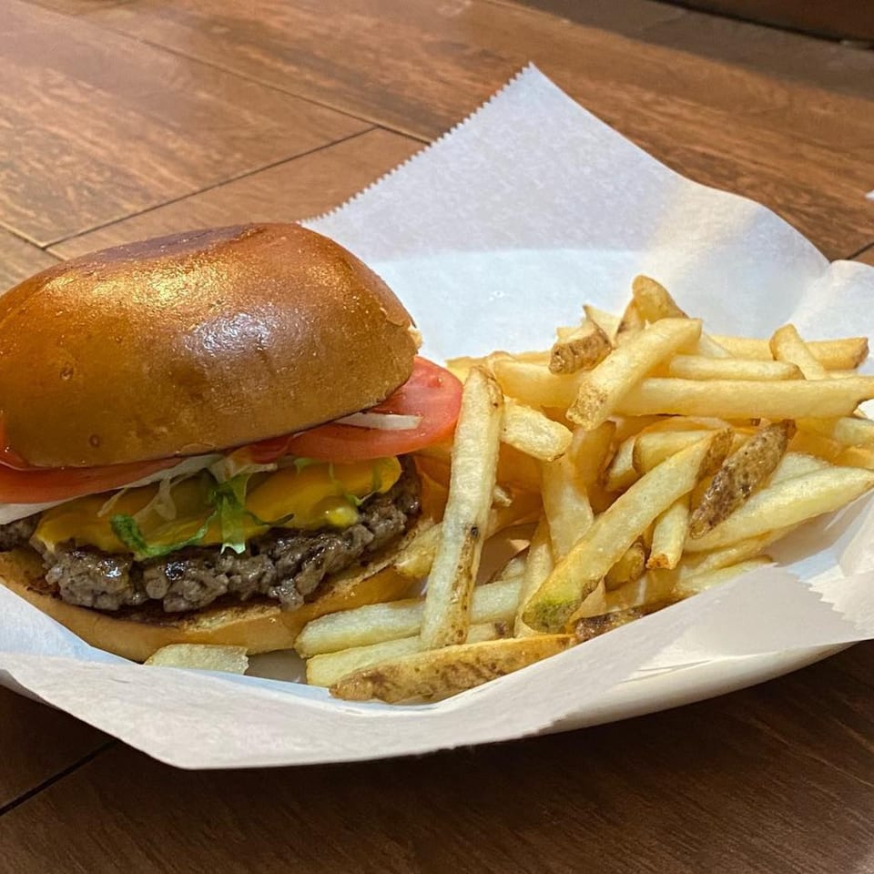 A cheeseburger with lettuce, tomato, and onion, served with a side of golden french fries.