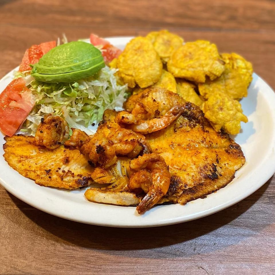 El Pastor's grilled fish and shrimp with plantains, avocado, and salad on a white plate.