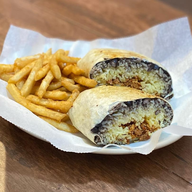 A cut burrito filled with rice, beans, and meat, served with a side of golden french fries.