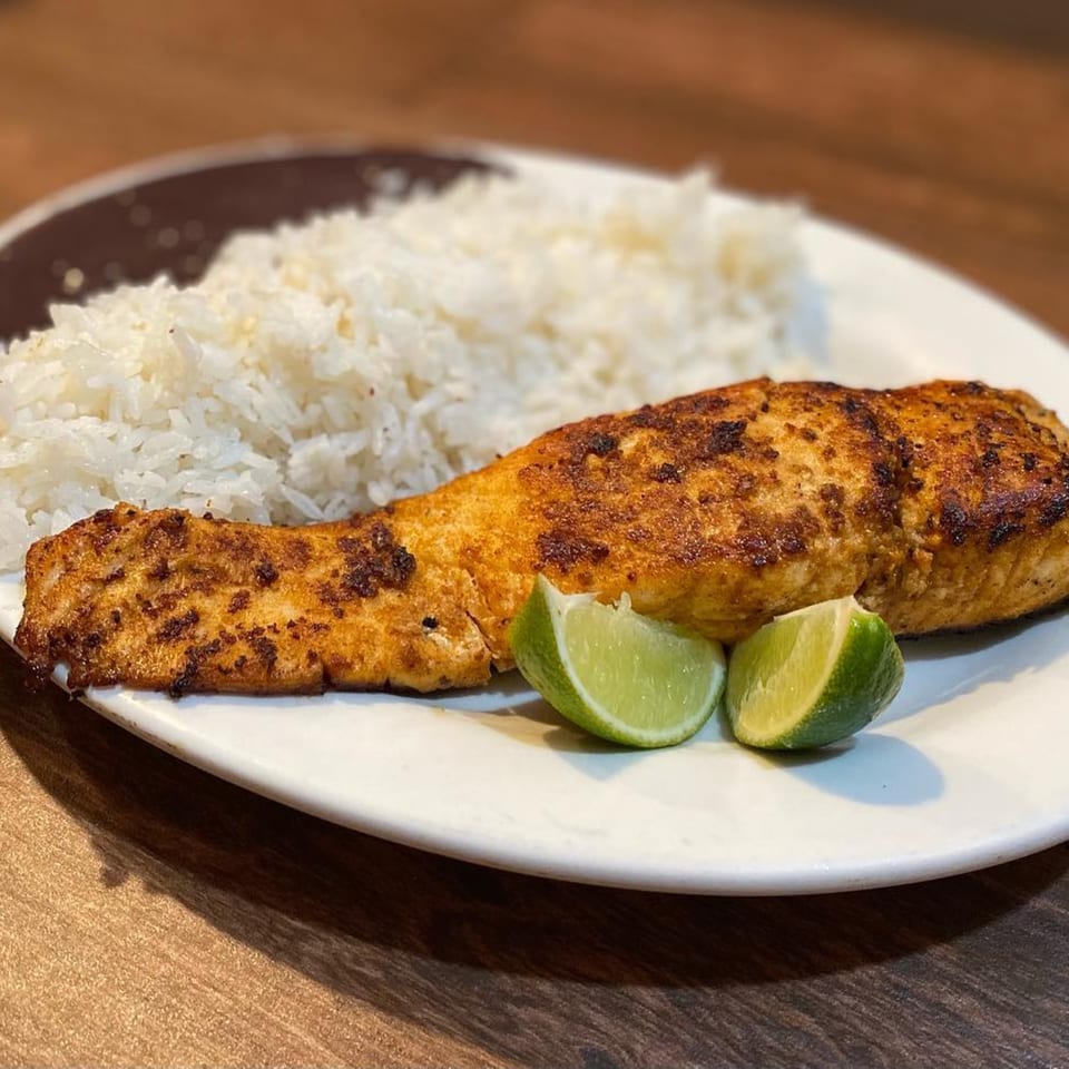 Grilled salmon with crispy skin, white rice, and two lime wedges on a white plate.